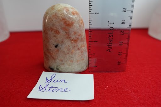 A piece of orange and white stone with ruler on red cloth