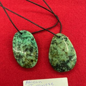 A pair of green stone pendants on a red surface