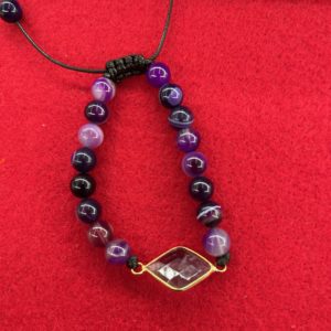 A bracelet with purple and black beads on a red surface