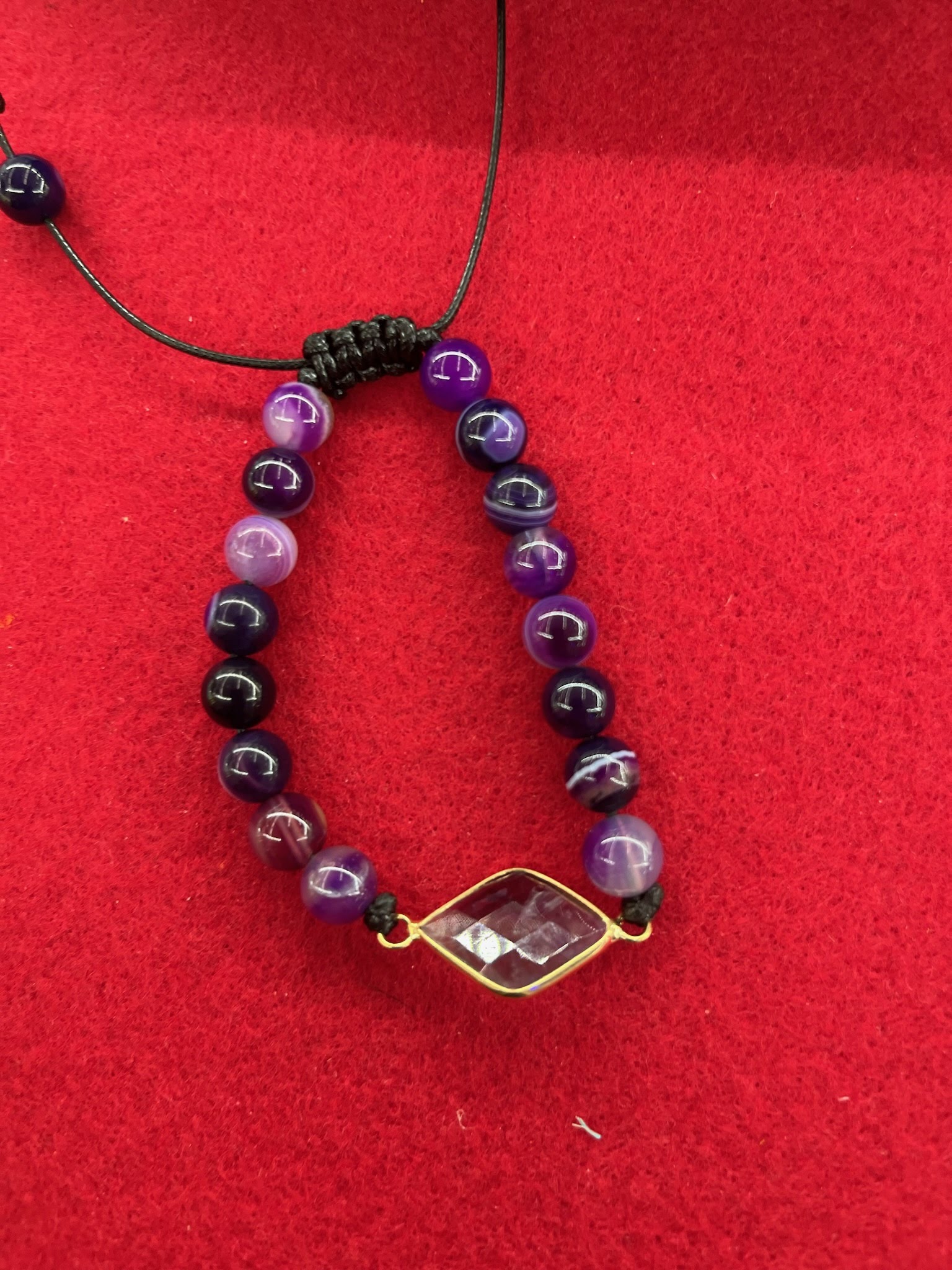 A bracelet with purple and black beads on a red surface