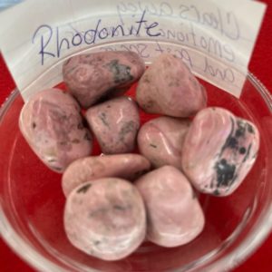 A bowl of rhodonite rocks with a note on the side.